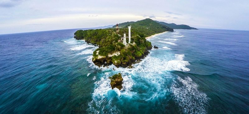 Aerial view of a coastal lighthouse on a rocky island surrounded by waves