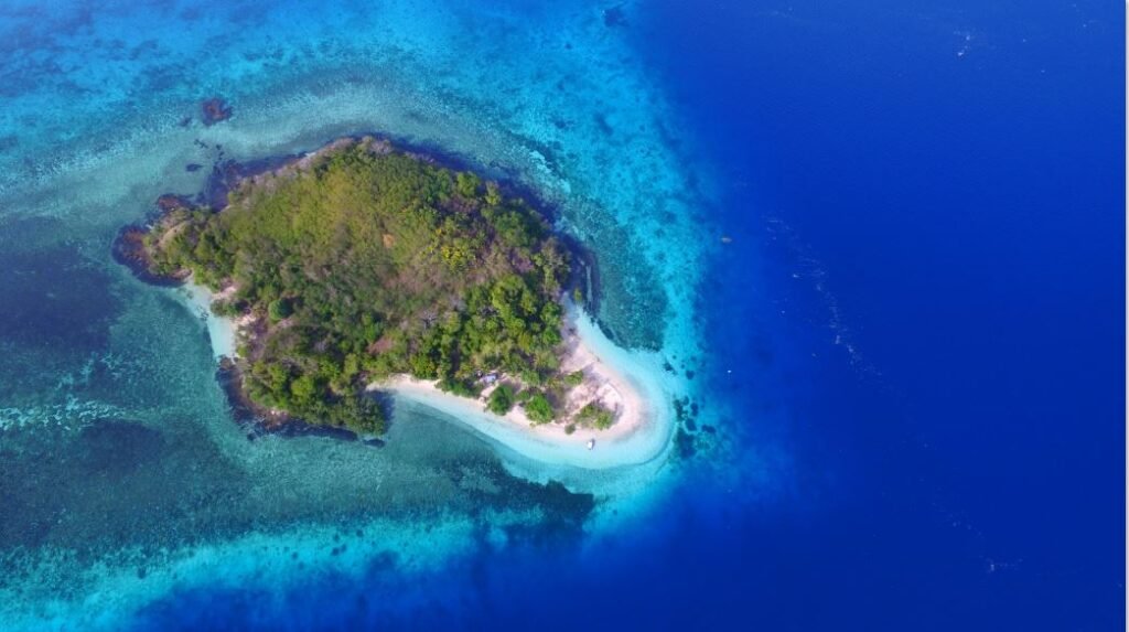 Aerial view of a small tropical island with white sandy beach and vibrant blue surrounding water