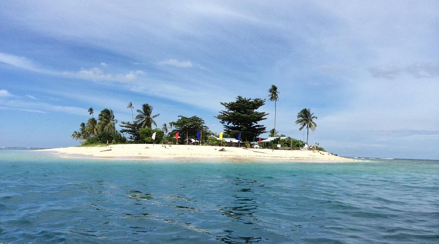 Small tropical island with white sandy beach and palm trees surrounded by clear blue water