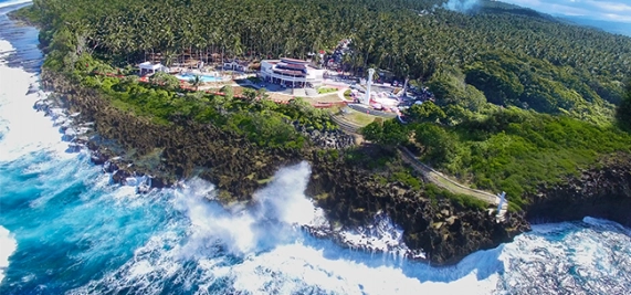 Aerial view of a cliffside resort with lush greenery and waves crashing against rocks